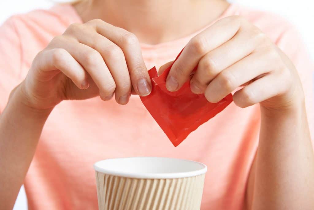woman adding artificial sweetener to a drink