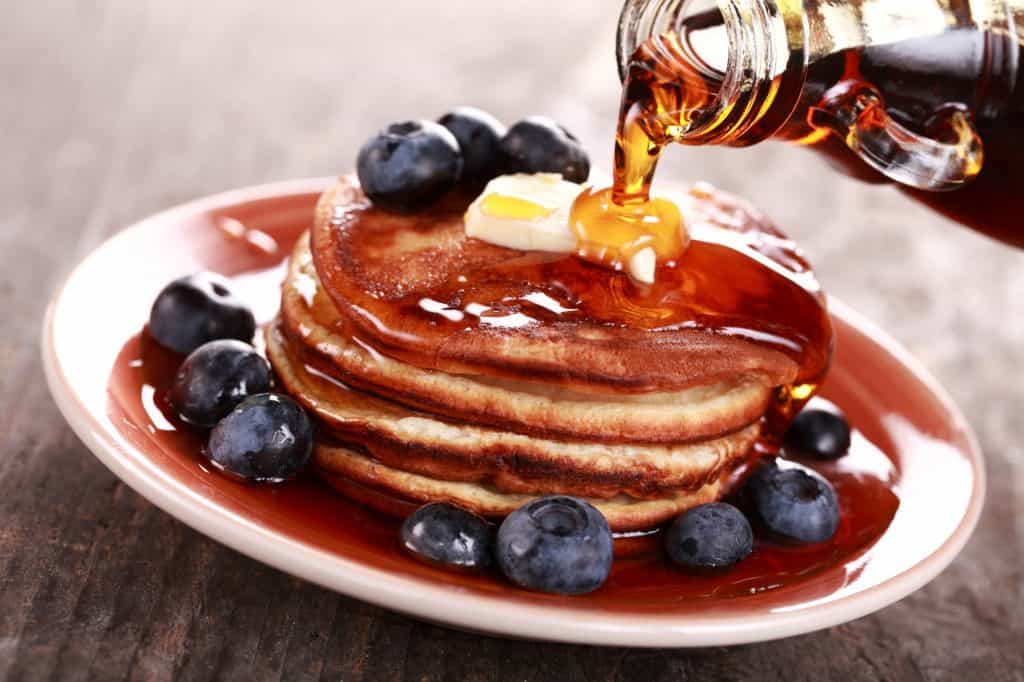 pouring maple syrup on a stack of pancakes