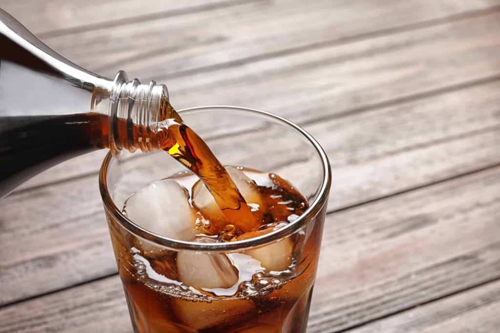 pouring soda from a bottle into a glass with ice