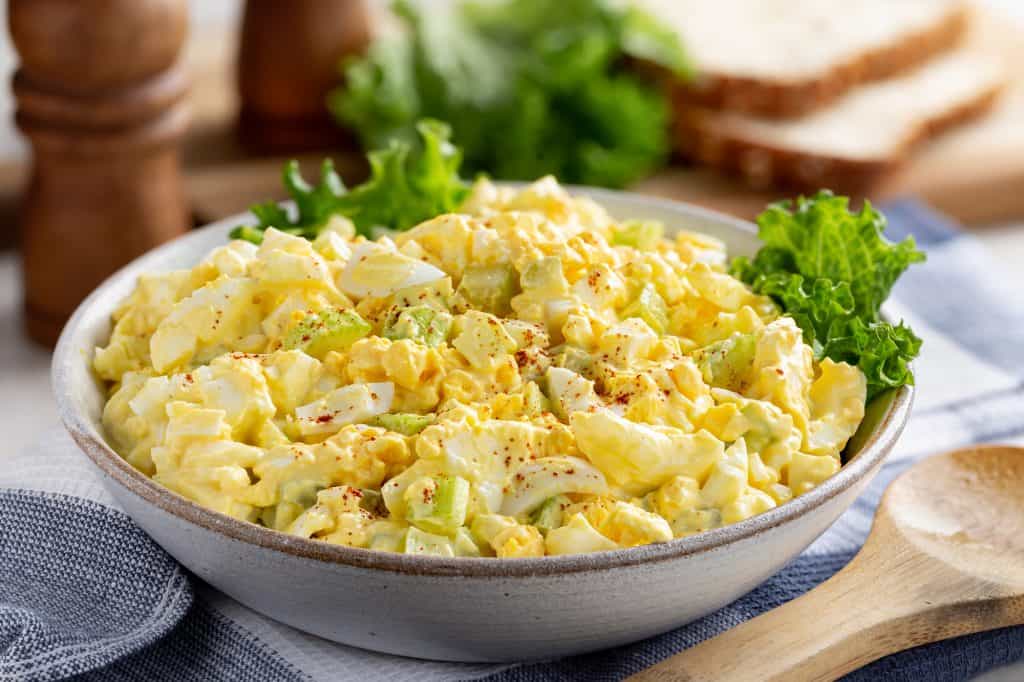 Egg salad in a bowl with bread slices and lettuce
